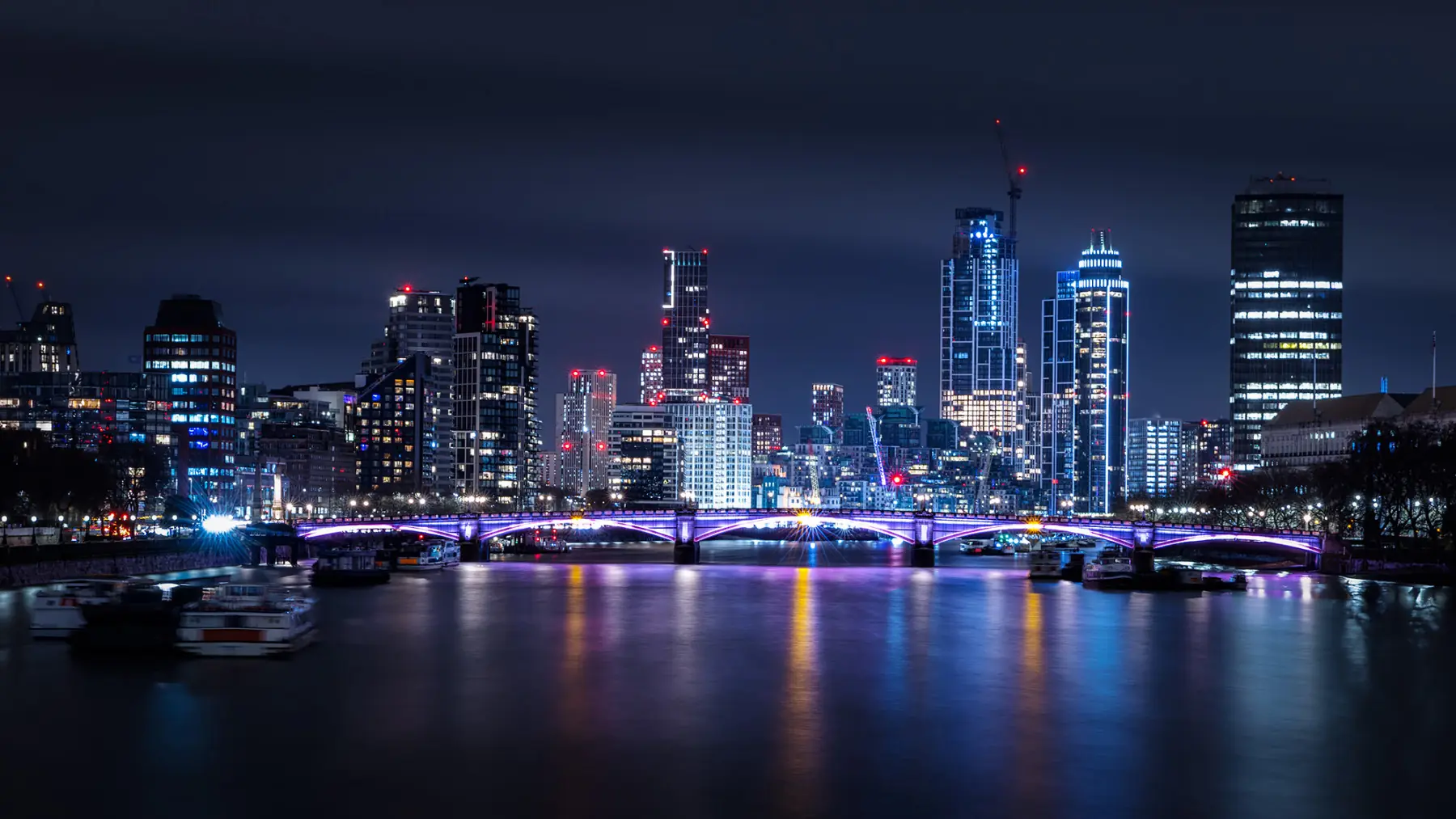 The London skyline at night across the Thames, towers lit against a dark sky.